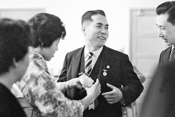 Kaneko, esposa de Ikeda sensei, coloca distintivo com a inscrição “presidente” em sua lapela antes de ele se encaminhar para a cerimônia de posse como terceiro presidente da Soka Gakkai. A partir daí, iniciou-se um novo avanço grandioso do kosen-rufu (auditório da Universidade Nihon, em Tóquio, 3 maio 1960)