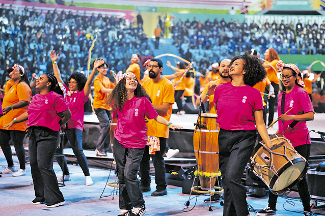 foto de jovens cantando e dançando em meio ao palco da convenção da juventude soka de maio, no ginásio do ibirapuera, um local coberto e circular com arquibancadas no entorno