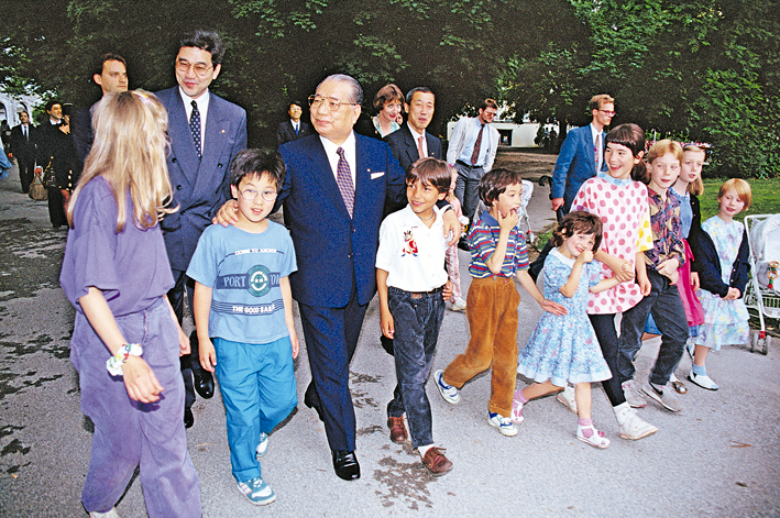 foto de Daisaku Ikeda caminhando em um espaço aberto ao lado de crianças e dois adultos 